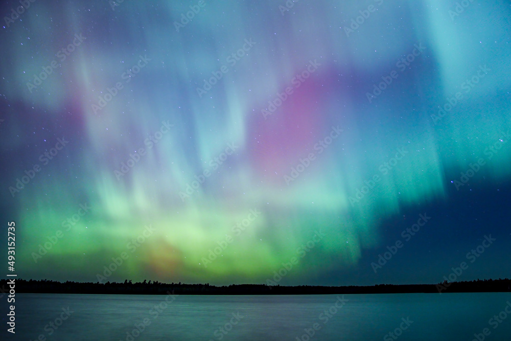 Northern lights erupt over remote Minnesota lake at night with rainbow of color shining off water Aurora Borealis nature show