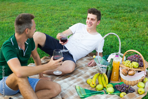 Two happy french males friends gaily spending time together on picnic drinking wine. © JackF