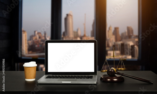 Workspace of lawyer with laptop blank white screen and law wooden gavel, and brass scale of judge.