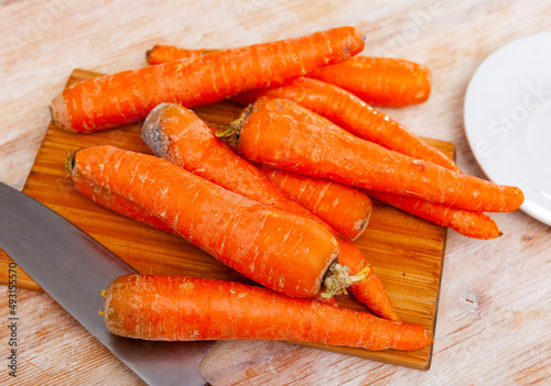 Fresh organic carrots on a wooden cutting kitchen board with kitchen knife