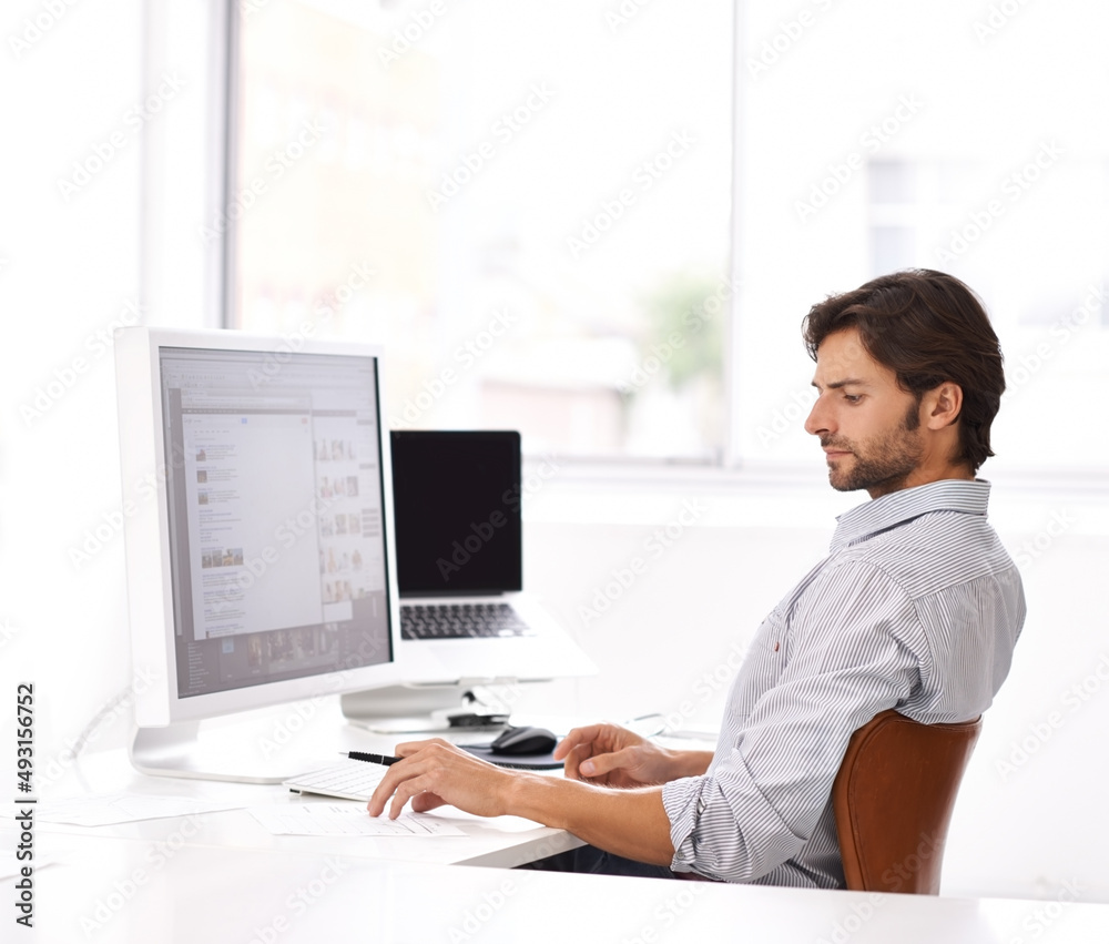 Never far from his workstation. A handsome young man at his desk in an office. Never far from his workstation. A handsome young man at his desk in an office.