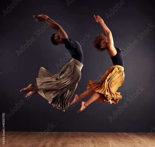 Synchronisity. Two contemporary dancers performing a synchronized leap in front of a dark background. photo