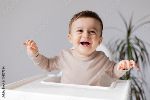 cheerful smiling baby is sitting in a white high chair for feeding. white background