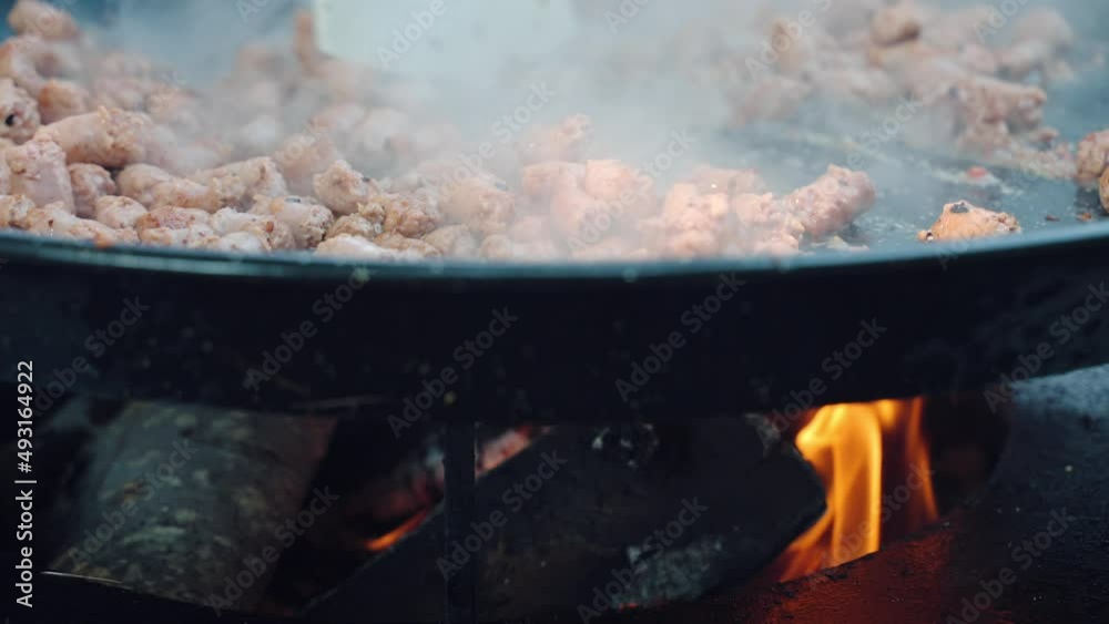 Street food preparation, sausages frying on big cauldron with fried vegetables on burning fire. Stewed and smoking sausages in barbecue saucepan, cookout concept Street food preparation, sausages frying on big cauldron with fried vegetables on burning fire. Stewed and smoking sausages in barbecue saucepan, cookout concept