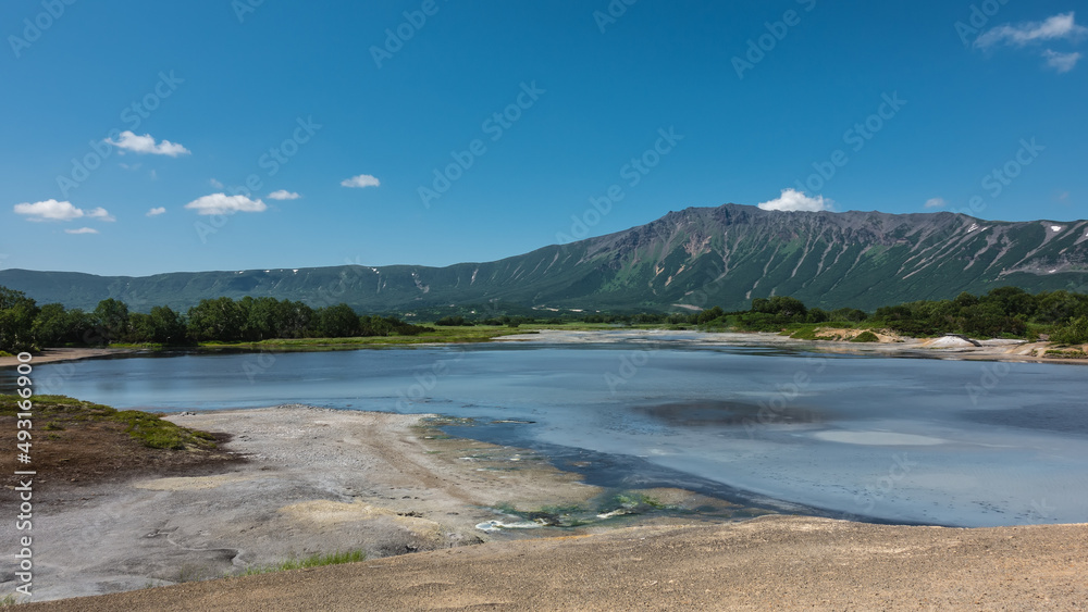 The caldera of an extinct volcano has a turquoise thermal lake with opaque water. Sulphurous deposits on the shores. A picturesque mountain range against a background of blue sky. Kamchatka. Uzon The caldera of an extinct volcano has a turquoise thermal lake with opaque water. Sulphurous deposits on the shores. A picturesque mountain range against a background of blue sky. Kamchatka. Uzon