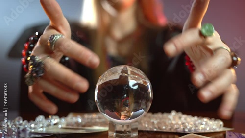 Occult witch gesturing with hands above small crystal sphere making predictions about future and connection with dark afterlife photo