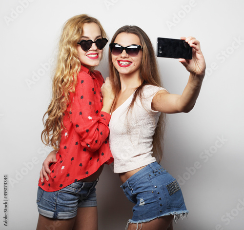 friendship, people and technology concept -two happy young women with smartphone taking selfie over white background