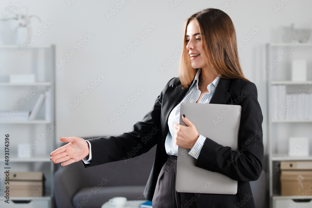Portrait of business woman with laptop giving hand at workplace in the office. Secretary welcome handshake, greeting interview. Relationship with business partner. Portrait of business woman with laptop giving hand at workplace in the office. Secretary welcome handshake, greeting interview. Relationship with business partner.