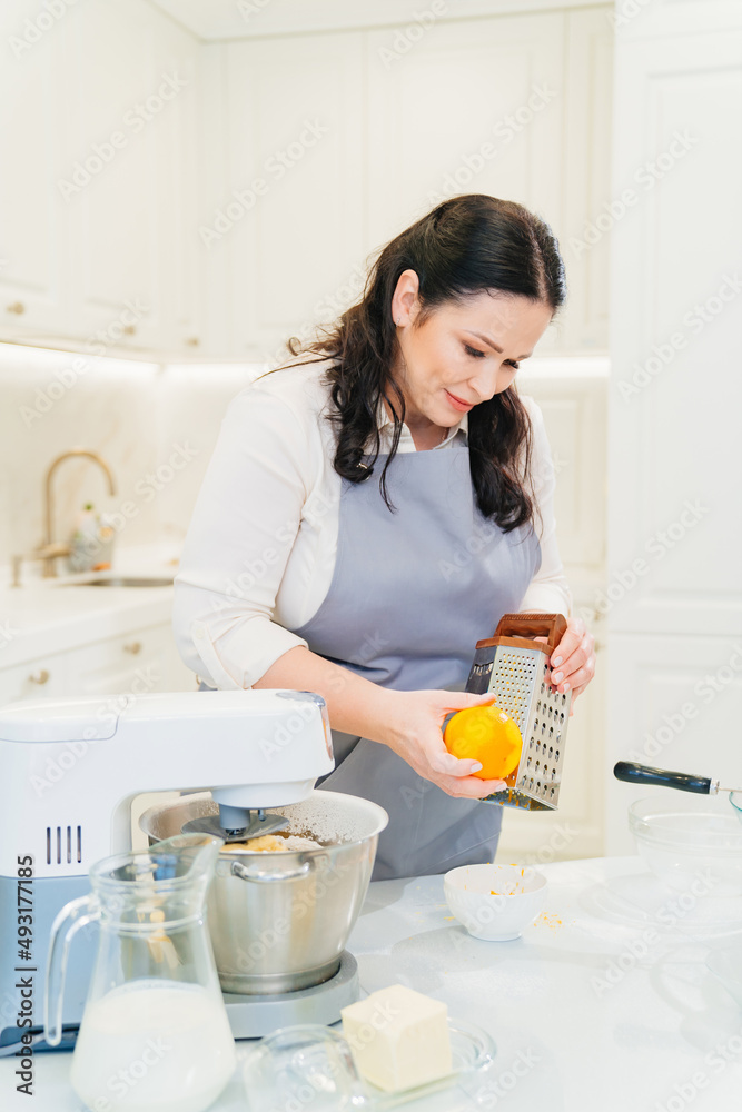 a woman cook makes orange zest on a grater to make pastries or cream. a woman cook makes orange zest on a grater to make pastries or cream.