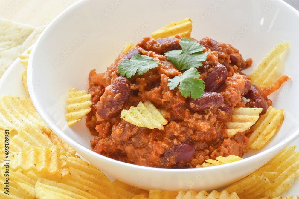 Chilli con carne with potato crisps in a white bowl. Traditional Mexican food. Chilli con carne with potato crisps in a white bowl. Traditional Mexican food.