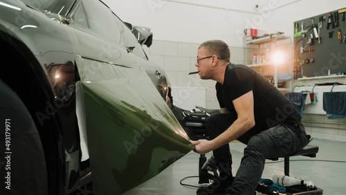 Close up shot of man vinyl wrapping the car door, pulling the film down. Process of vinyl wrapping a car using heat gun. Green vinyl film for car wrapping. High quality 4k footage