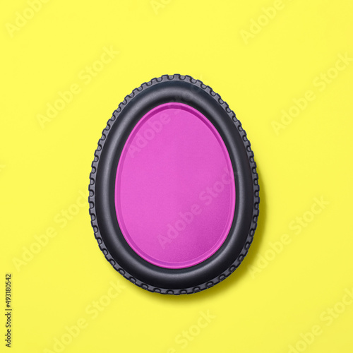 Egg shape made of car tire on a bright yellow background  with a pink fill. Minimal easter concept.  Flat lay.