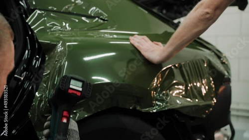 Two men are vinyl wrapping a car in dark green color. Process of vinyl wrapping a car in a car studio, using heat gun to stretch the film. Dark green car vinyl wrap. High quality 4k footage photo