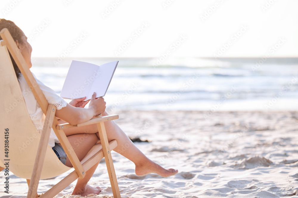 Nothing like the ocean and a good book. Shot of an unrecognizable woman reading a book at the beach.