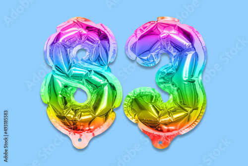 Rainbow foil balloon number, digit eighty three on a blue background. Birthday greeting card with inscription 83. Top view. Numerical digit. Celebration event, template.