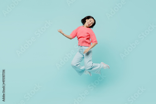 Full body young smiling singer happy woman of Asian ethnicity 20s in pink sweater jump high paly guitar isolated on pastel plain light blue color background studio portrait. People lifestyle concept.