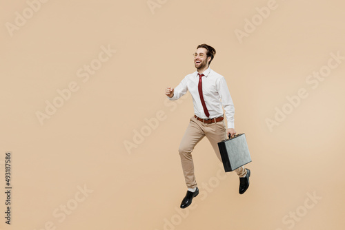 Full body young successful employee business man corporate lawyer 20s wear white shirt red tie glasses work in office jump run fast hold briefcase isolated on plain beige background studio portrait.
