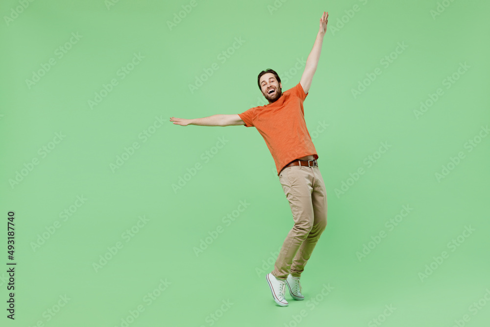Full body young man 20s wear casual orange t-shirt dancing stand on toes leaning back fooling around isolated on plain pastel light green color background studio portrait. People lifestyle concept