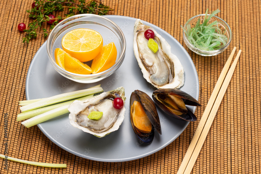 Clams and oysters in shells, lemon in bowl and celery stalks on gray bowl