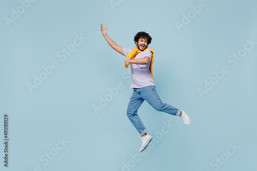 Full size body length amazing happy young bearded Indian man 20s years old wears white t-shirt singing song dreaming like playing guitar isolated on plain pastel light blue background studio portrait.
