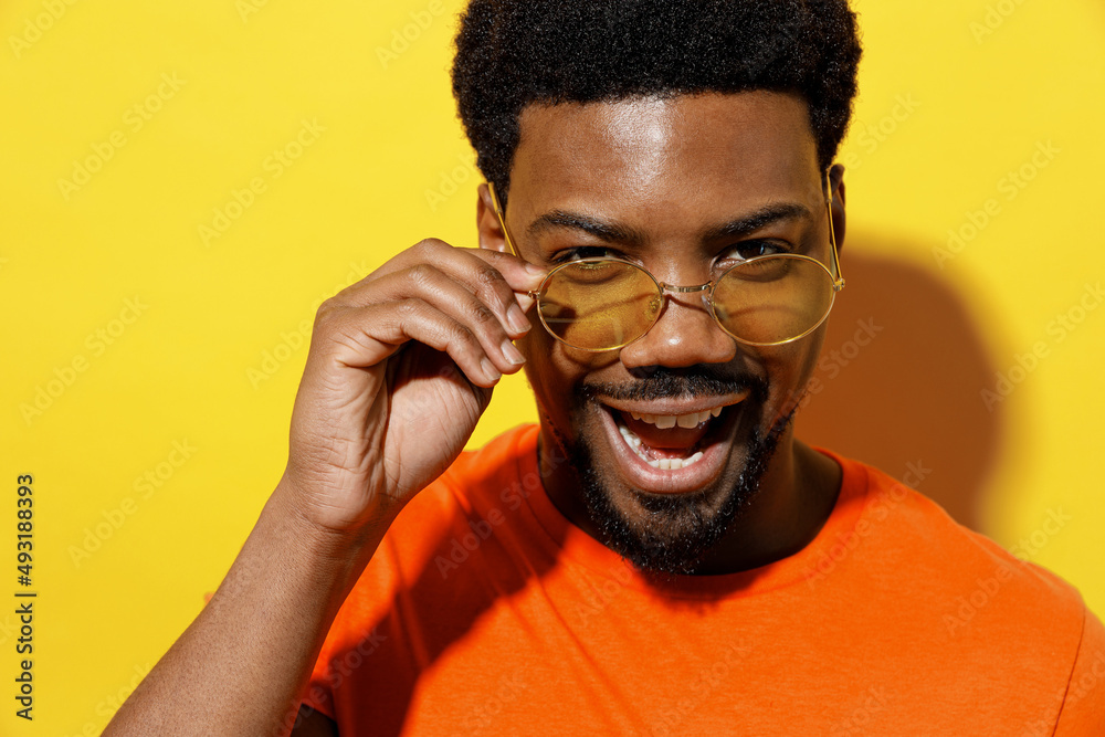 Obraz premium Close up young cool man of African American ethnicity 20s in basic casual orange t-shirt take off glasses listen music in earphones isolated on plain yellow background studio People lifestyle concept