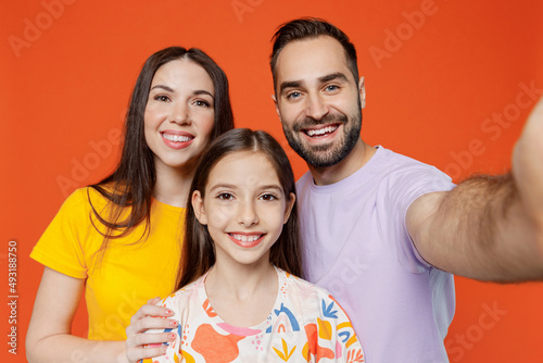 Close up young happy parents mom dad with child kid daughter teen girl in basic t-shirts doing selfie shot pov on mobile phone isolated on yellow background. Family day parenthood childhood concept
