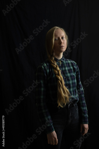 A young Ukrainian woman blonde with a braided braid in the studio on a black isolated background and a pendant Trident. The concept of stop war in Ukraine from the Russian invaders