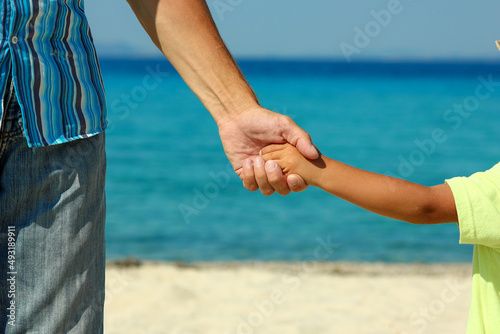 The parent holds the child's hand on the beach
