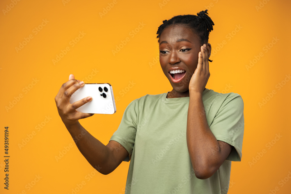 Happy smiling african american girl using her smartphone in yellow studio.