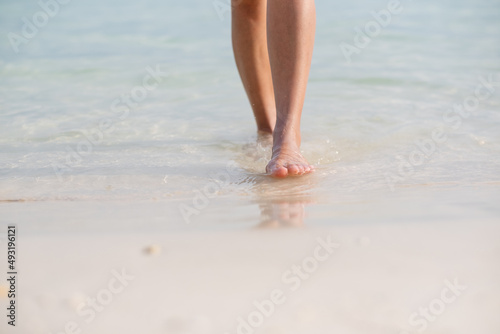 Closeup image of woman with barefoot while walking on the white beach and the sea