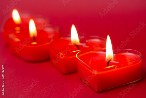 Four red burning heart-shaped candles with blazing flames. Tongues of fire on a red background. Valentine s Day  passion  love  feelings concept. Monochrome wallpaper. I love you decor for February 14