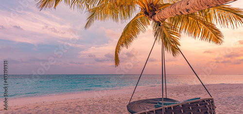 Tropical sunset beach panorama as summer landscape with relax beach swing or hammock on coconut palm, white sand and calm sea beach banner. Perfect beach vacation or summer holiday panoramic concept © icemanphotos