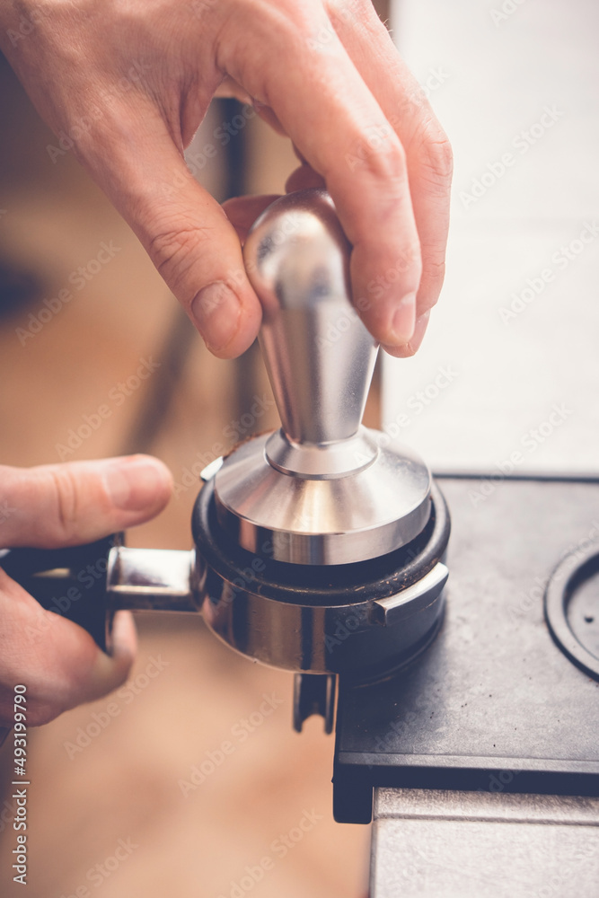 Obraz premium Barista tampering coffee in portafilter using tamper. Close-up fresh coffee preparation process