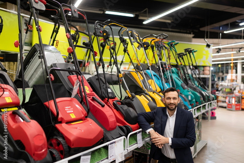 Owner of a gardening power tool store next to a display case with rechargeable electric lawn mowers me