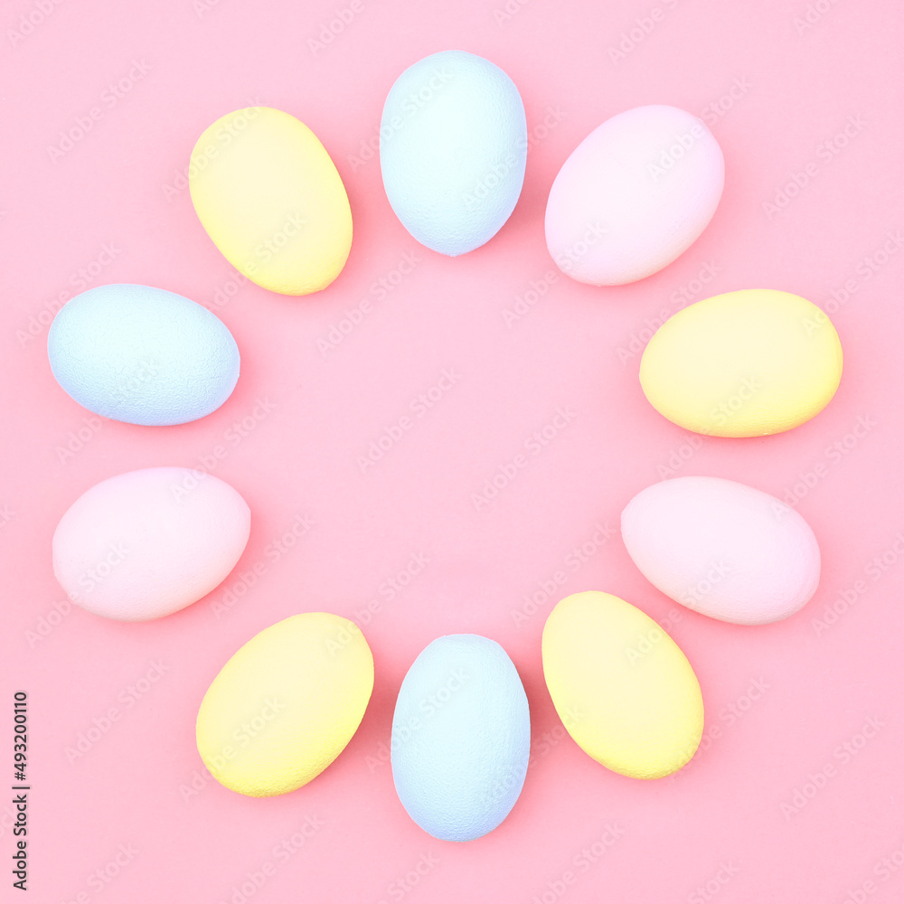 Creative Easter layout made of colorful eggs and flowers on a pink background. Circle wreath of easter eggs flat concept.