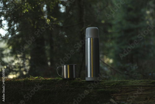 Thermos and cup on log in forest