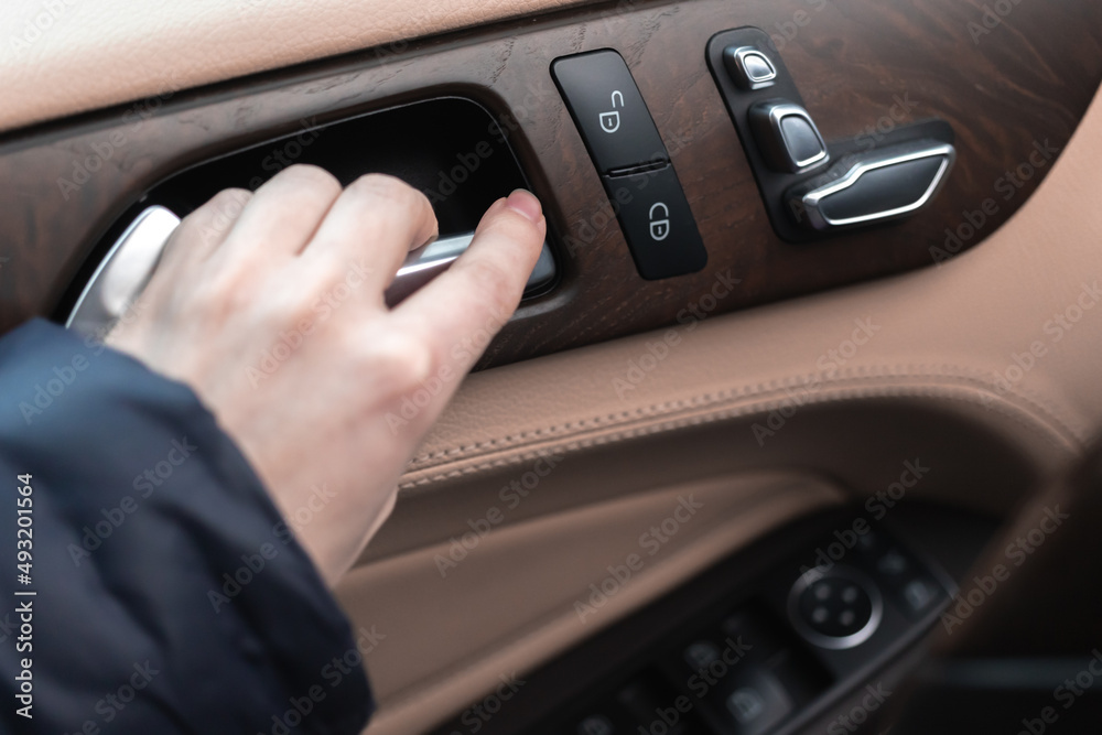 Hand with car door handle inside the luxury car interior with leather and wood design. Close-up view photo