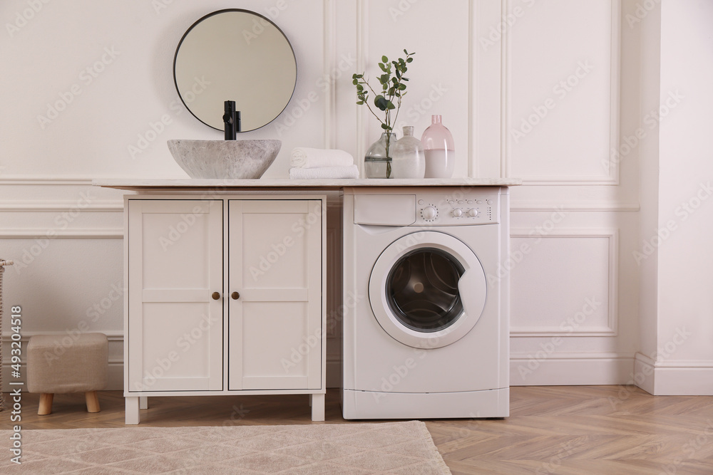 Laundry room interior with modern washing machine and stylish vessel sink on countertop