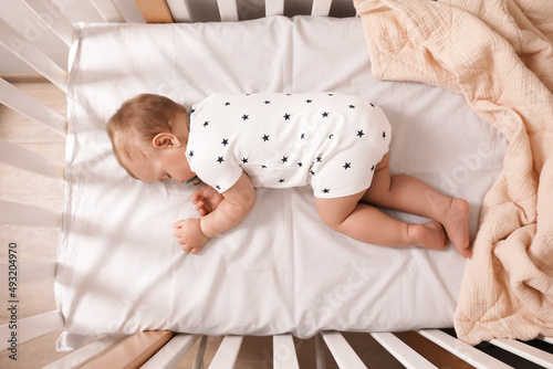 Adorable little baby with pacifier sleeping in crib indoors, top view photo