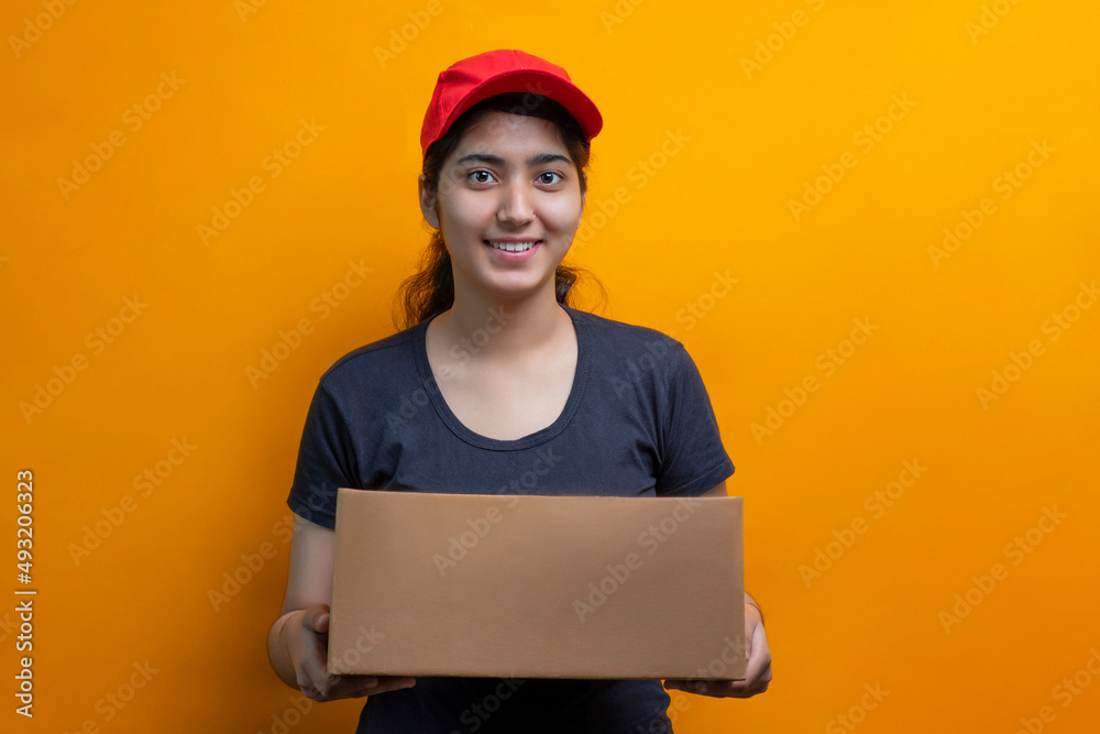 Young Delivery Woman Holding Cardboard Box Against Yellow Background Young Delivery Woman Holding Cardboard Box Against Yellow Background