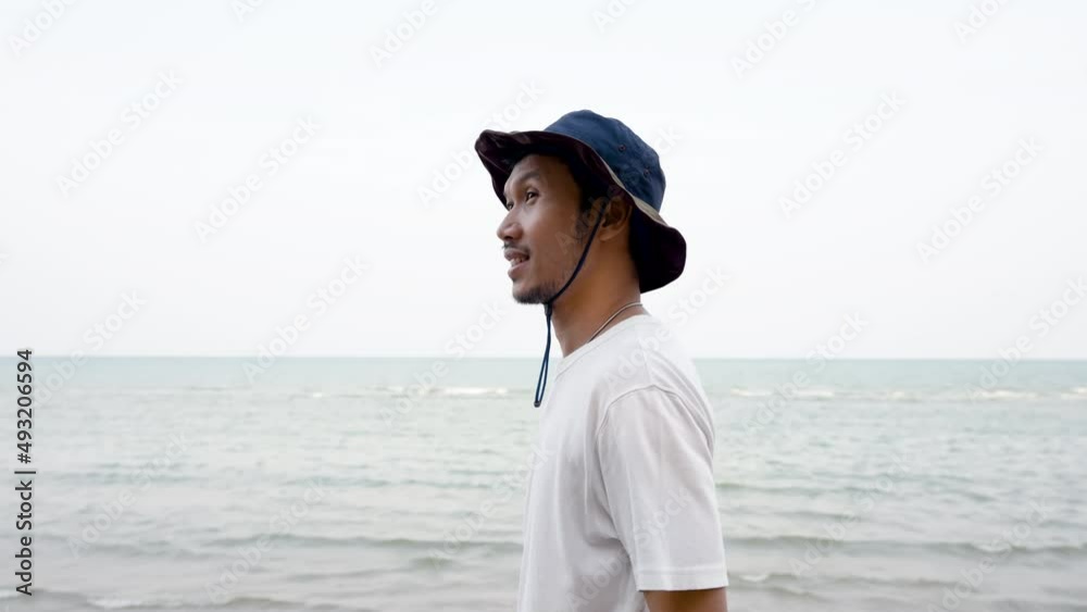 4K 50fps, a Nice looking Asian man, wearing a white shirt and his favorite hat, walking by the sea, smiling happily 4K 50fps, a Nice looking Asian man, wearing a white shirt and his favorite hat, walking by the sea, smiling happily