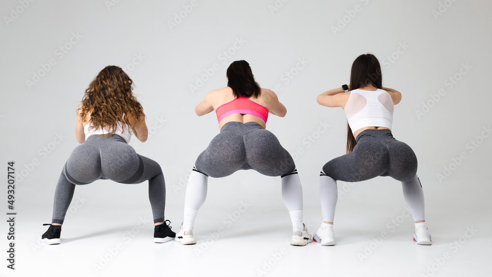 Three young fitness women squat in the studio. Girls with beautiful buttocks are doing a warm-up Three young fitness women squat in the studio. Girls with beautiful buttocks are doing a warm-up