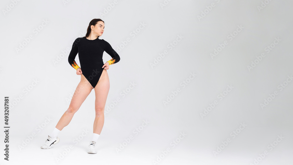 Attractive girl dancer in a black bodysuit posing in the studio on a white background