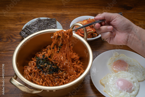 Hand using chopsticks to pick up Ramyeon noodle in a traditional korean noodle pot, Spicy Korean Ramyeon instant noodle a traditional dish.