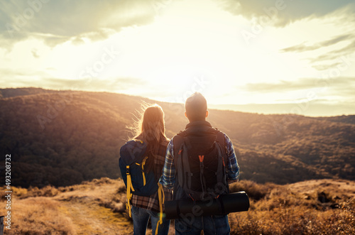 Rear view of couple with backpacks hiking together in nature on autumn day.