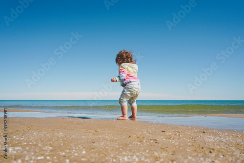 Wide view of a little girl wearing rainbow hoodie playing at the beach © nanihta