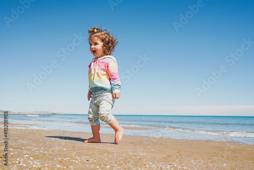 Wide view of a little girl wearing rainbow hoodie playing at the beach