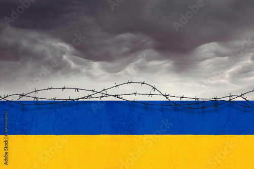 Muro con i colori della bandiera ucraina recintato da filo spinato sotto un cielo tempestoso. photo