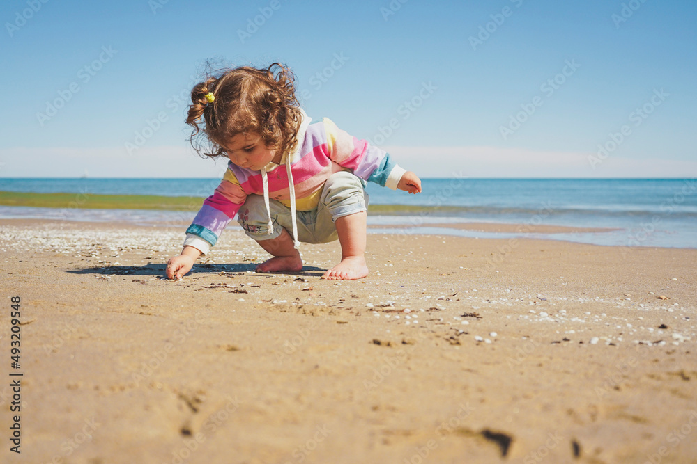 Wide view of a little girl wearing rainbow hoodie playing at the beach