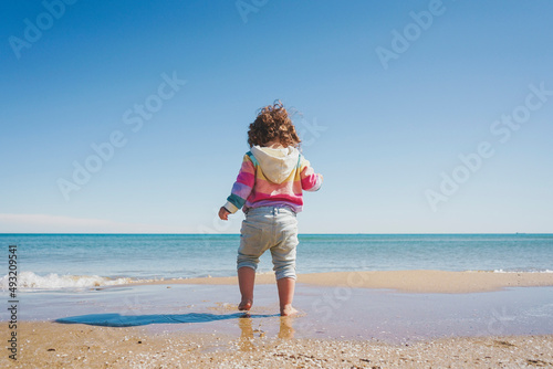 Wide view of a little girl wearing rainbow hoodie playing at the beach © nanihta